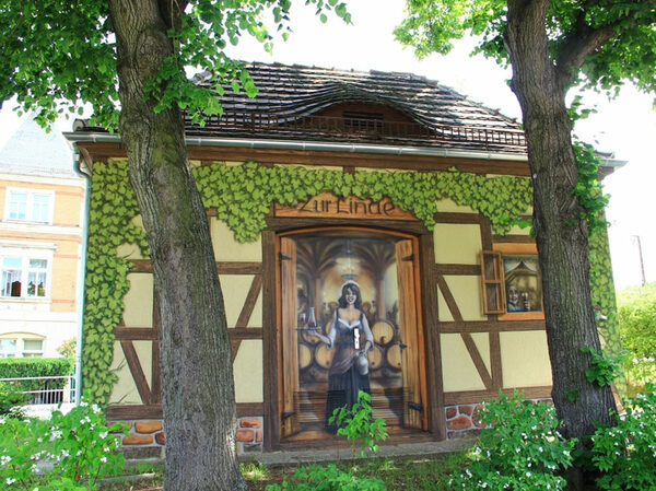 Das Foto zeigt eine kleine Station der DREWAG, welche mit einem Graffiti verziert ist auf welchem eine Szene aus der Schenke "Zur Linde" dargestellt ist.