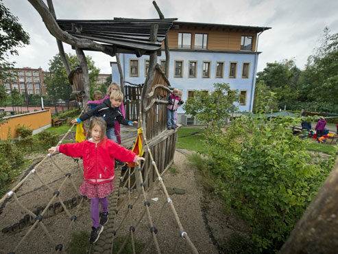 Bild zeigt die Freifläche der Kindertagesstätte Himmelblau Leisniger Straße 70. Kinder spielen am Klettergerüst.