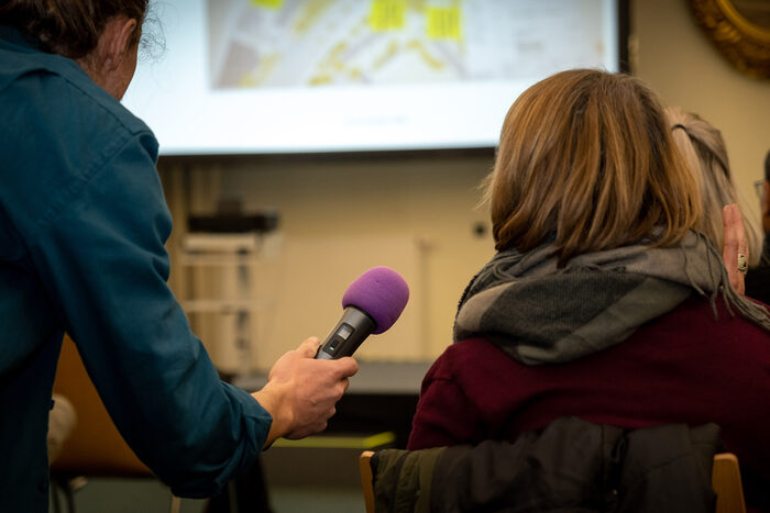 Zu sehen ist ein Mitarbeiter der Stadtverwaltung Dresden, der eine Bürgerin mit Mikrofon befragt.