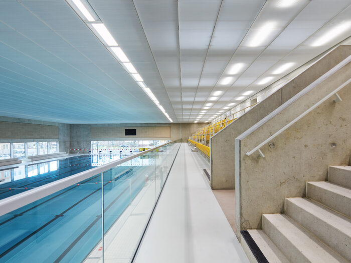 Auf dem Bild ist eine Innenaufnahme des neuen Schwimmkomplexes auf der Freiberger Straße zu sehen. Auf der linken Seite ist das Schwimmbecken zu sehen. Auf der rechten Seite befinden sich der Treppenaufgang und der Zuschauerrang.