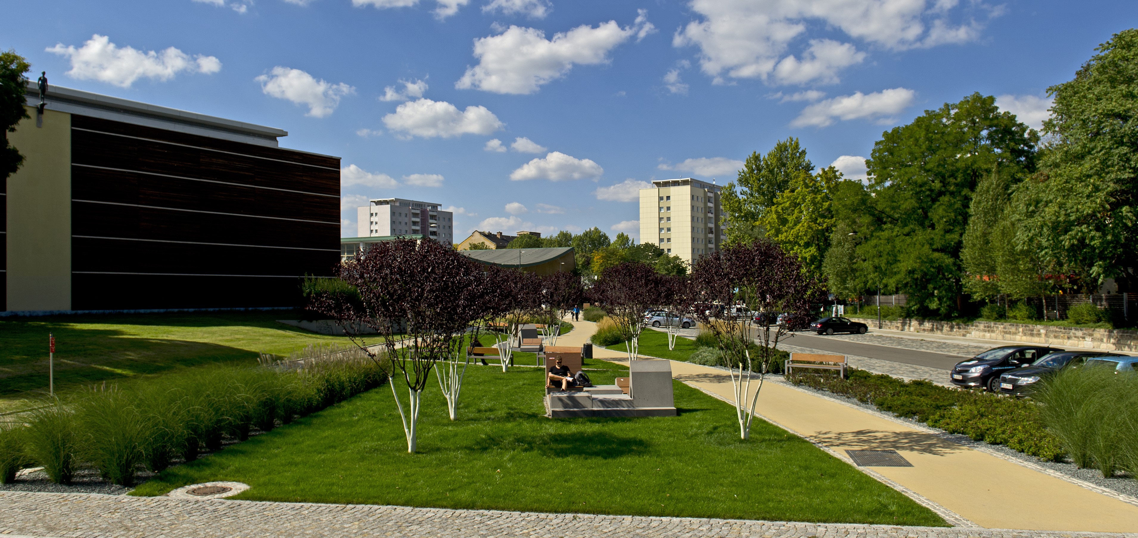 Zu sehen ist der Vorplatz des Schwimmsportkomplex Freiberger Straße mit Grünanlage und Sitzmöglichkeiten.