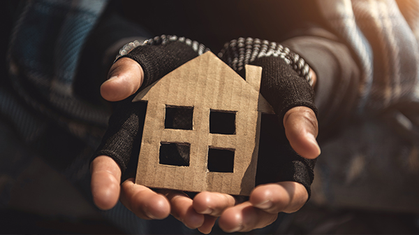 Hände in schwarzen Handschuhen halten ein aus Pappe ausgeschnittenes Haus