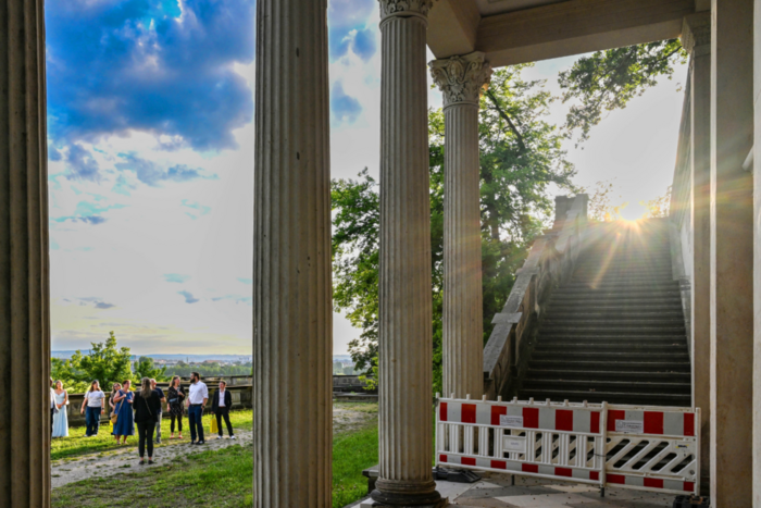 Menschen stehen im Abendlicht unter Säulen aus Sandstein.