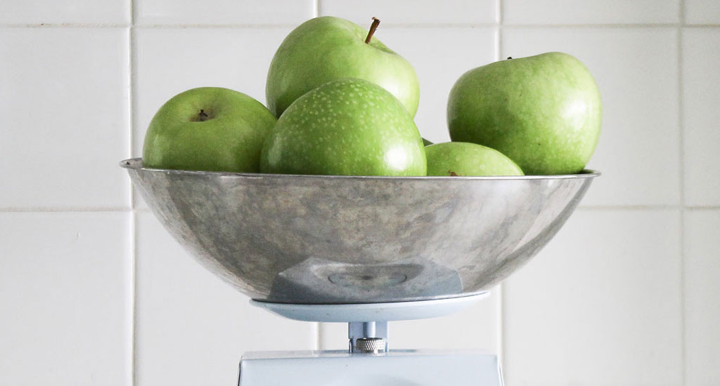 Photo of a bowl with six green apples on a scale