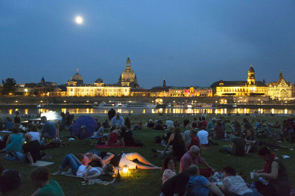 Junge Menschen sitzen abends an der Elbe mit Blick auf die Silhouette.