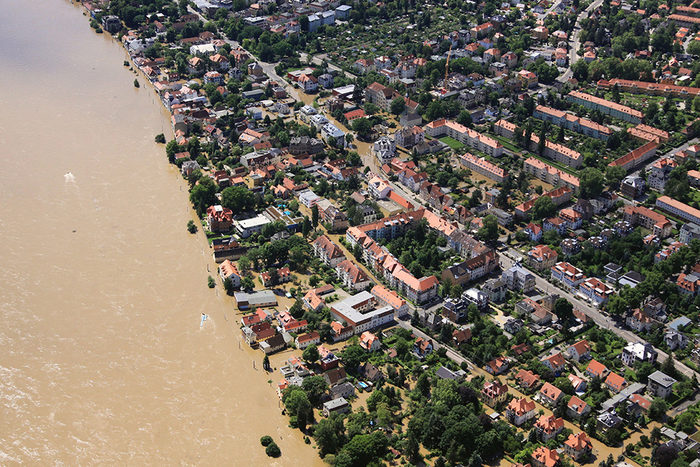 Luftbild von einem breitem Fluss und überfluteten Stadttvierteln