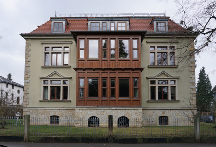Dreigeschossiges Einfamilienhaus mit rotem Mansarddach und hölzerner Loggia.