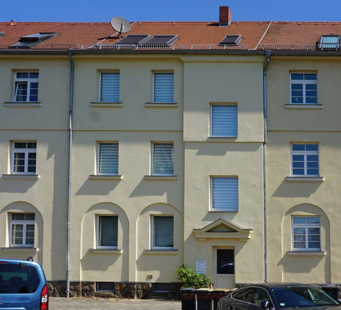 Viergeschossiges gelbes Mehrfamilienhaus mit rotem Satteldach.