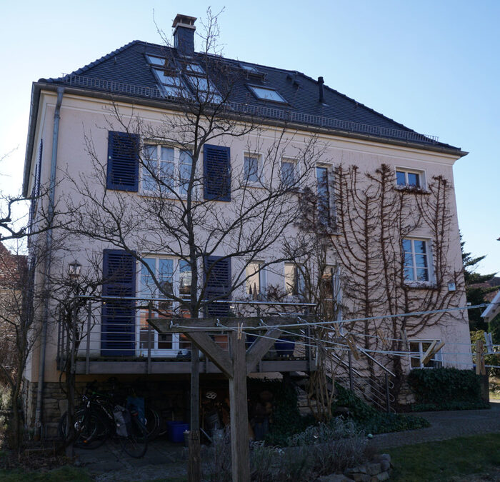 Zweigeschossiges Einfamilienhaus mit dunklem Walmdach und blauen Fensterläden.