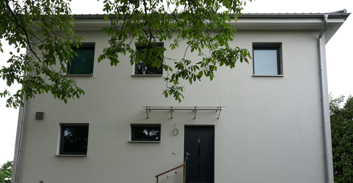 Modernes zweigeschossiges Einfamilienhaus mit großen Fenstern und flach geneigtes Dach.