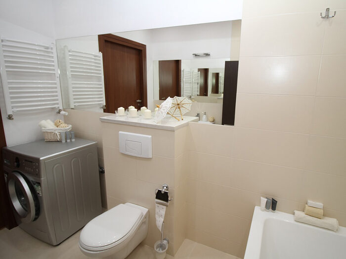 Foto von einem Bad mit einer Toilette, darüber einem Spiegel und einer Waschmaschine daneben.