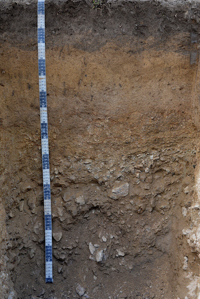 Ein Querschnitt des Erdbodens mit einem Lineal und verschiedenen Schichten.