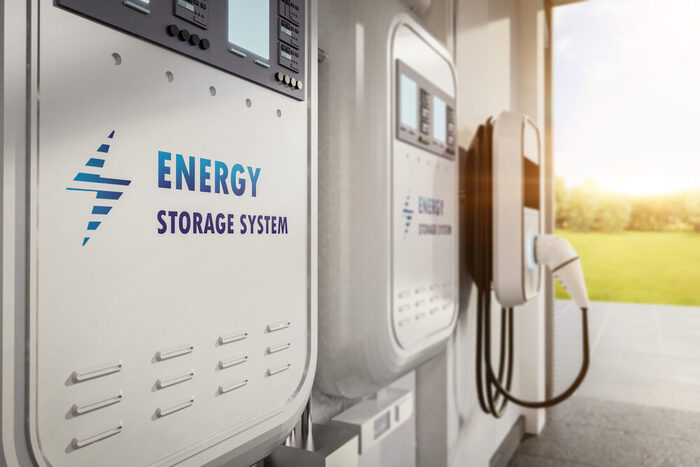 Die Abbildung zeigt einen Batteriespeicher in einer Garage neben eine Lademöglichkeit für E-Autos. Solche Systeme speichern überschüssige Energie, etwa aus Photovoltaikanlagen, und machen sie bei Bedarf verfügbar.