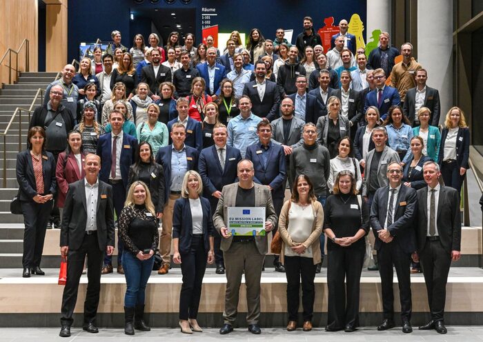 Die Teilnehmenden des Innovationsforums haben sich auf der Treppe im Foyer des Stadtforums zu einem Gruppenfoto mit EU-Label versammelt.