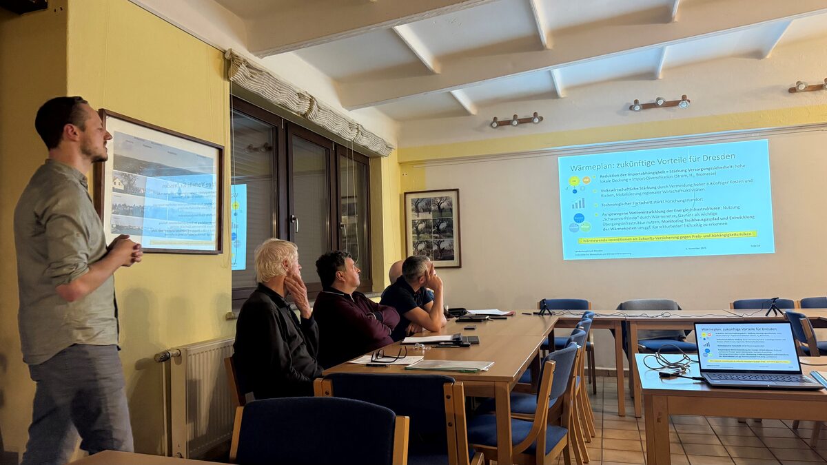 Während einer Sitzung des Stadtbezirksbeirats bzw. Ortschaftsrates wird die Kommunale Wärmeplanung der Landeshauptstadt Dresden vorgestellt. Mehrere Beiratsmitglieder sitzen an einem Tisch und verfolgen aufmerksam die Präsentation.