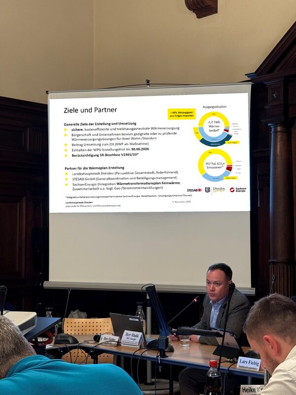 Während einer Sitzung des Stadtbezirksbeirats bzw. Ortschaftsrates wird die Kommunale Wärmeplanung der Landeshauptstadt Dresden vorgestellt. Mehrere Beiratsmitglieder sitzen an einem Tisch und verfolgen aufmerksam die Präsentation.