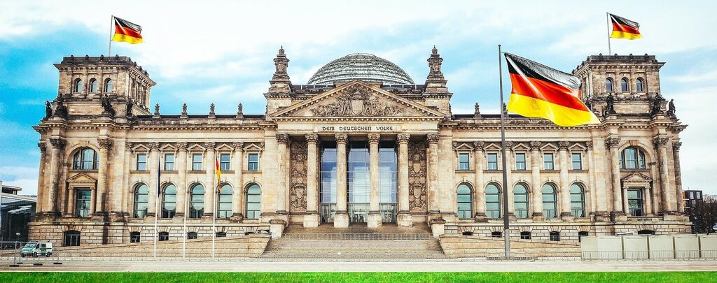 Der Deutsche Bundestag von außen. Vor dem Gebäude und auf den Dächern wehen Deutschlandfahnen.