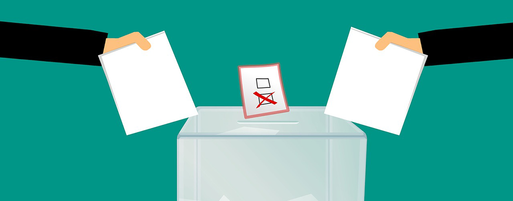 Zwei Hände stecken von der Seite einen Stimmzettel in die Wahlurne