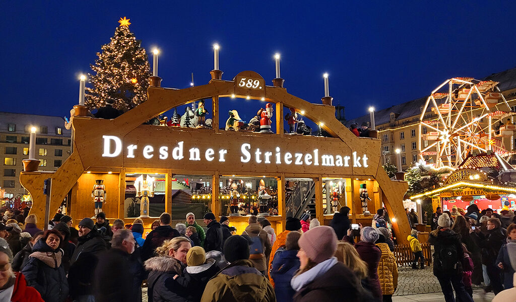 Blick auf den begehbaren Schwibbogen des Dresdner Striezelmarktes, dahinter Baum und Riesenrad