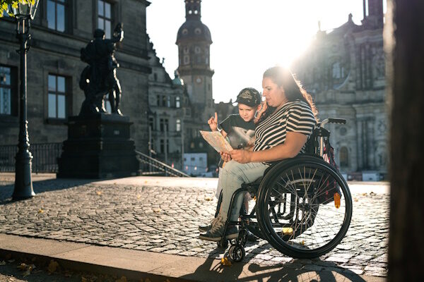 Auf der Brühlschen Terrase schauen Mutter und Kind gemeinsam in einen Stadtplan. Die Mutter sitzt im Rollstuhl.