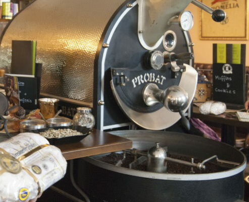 Große Kaffeemühle gefüllt mit braunen Bohnen. Im Vordergrund wird außerdem ein eingepackter Stollen in die Kamera gehalten.