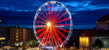 Das Riesenrad bei Nacht in leuchtend roten Farben vor dem wolkigen, fast schwarzen Himmel.