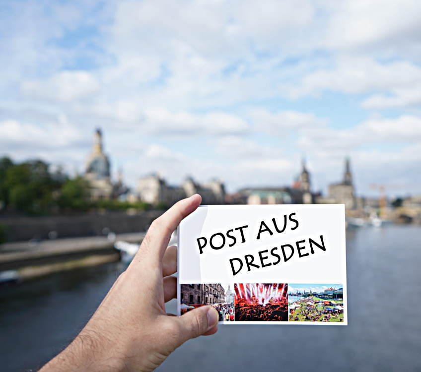 Eine Postkarte wird von einer Hand gehalten. Im Hintergrund sieht man verschwommen die Brühlsche Terrasse.