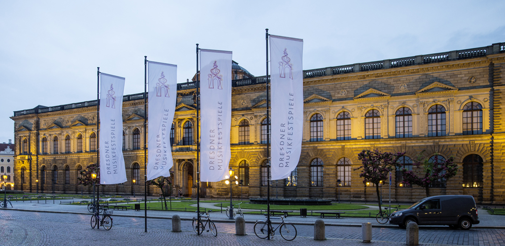 Vier Fahnen welche die Dresdner Musikfestspiele bewerben, im Hintergrund die Dresdner Semperoper erleuchtet in der Abenddämmerung