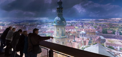 Пять человек стоят на платформе с перилами и смотрят на большую панораму Дрездена в эпоху барокко. Человек на самом фронте указывает рукой на Старый город с Цвингером.
