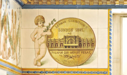 Detailaufnahme der verzierten Wandfliesen in der Pfunds Molkerei; nackter Knabe lehnt an goldenem Geldstück