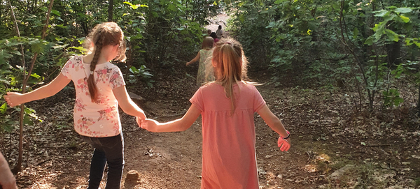 Zwei Mädchen gehen Hand in Hand durch einen Wald