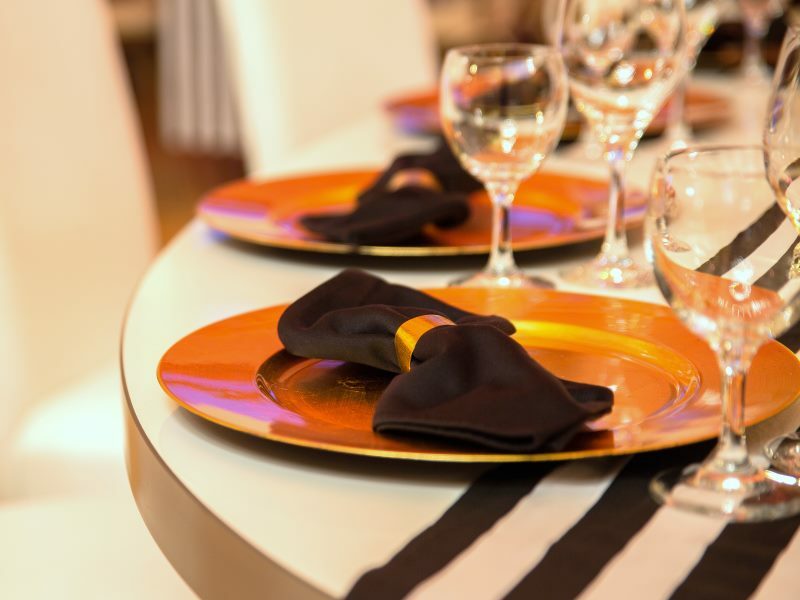 Gedeckter Tisch mit schwarzen Streifen, goldenen Tellern und schwarzen Servietten sowie Gläsern.